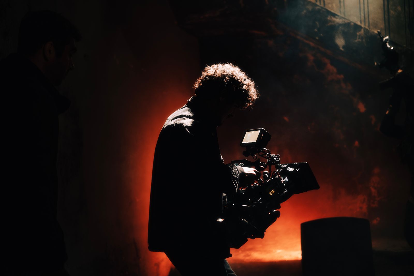 A camera operator silhouetted against warm stage light